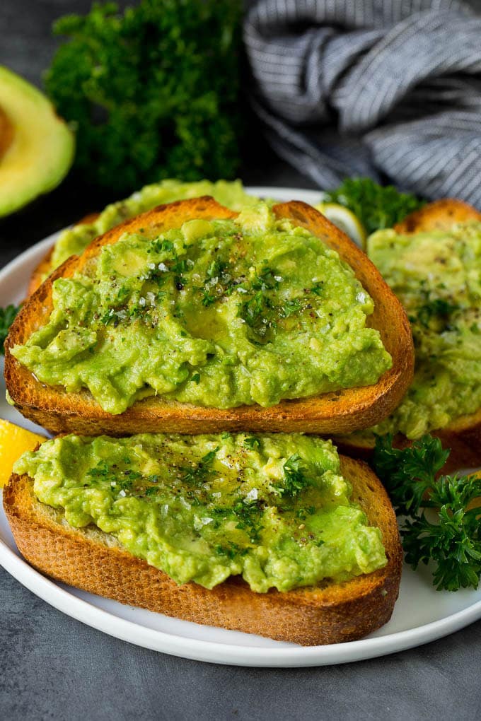 A plate of avocado toast with fresh parsley as a garnish.