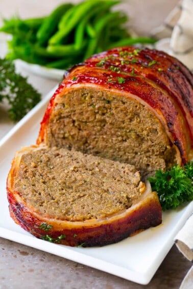 A bacon wrapped meatloaf with a slice out of it, on a serving platter.