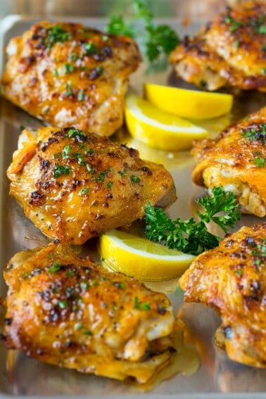 A pan of baked chicken thighs garnished with parsley and lemon.