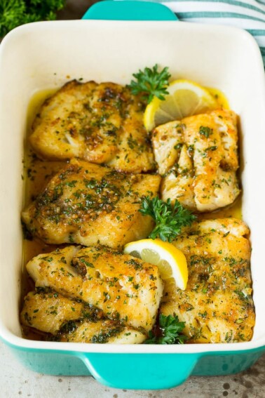 A pan of baked cod garnished with lemon and parsley.