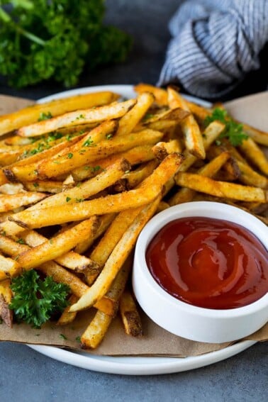 A plate of baked french fries served with ketchup.