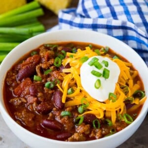 A bowl of beef chili topped with cheese, sour cream and green onions.