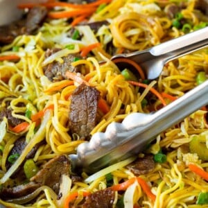 Tongs serving up a portion of beef chow mein.