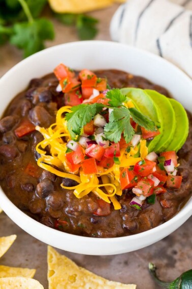 A bowl of black bean soup topped with salsa, avocado and cheese.