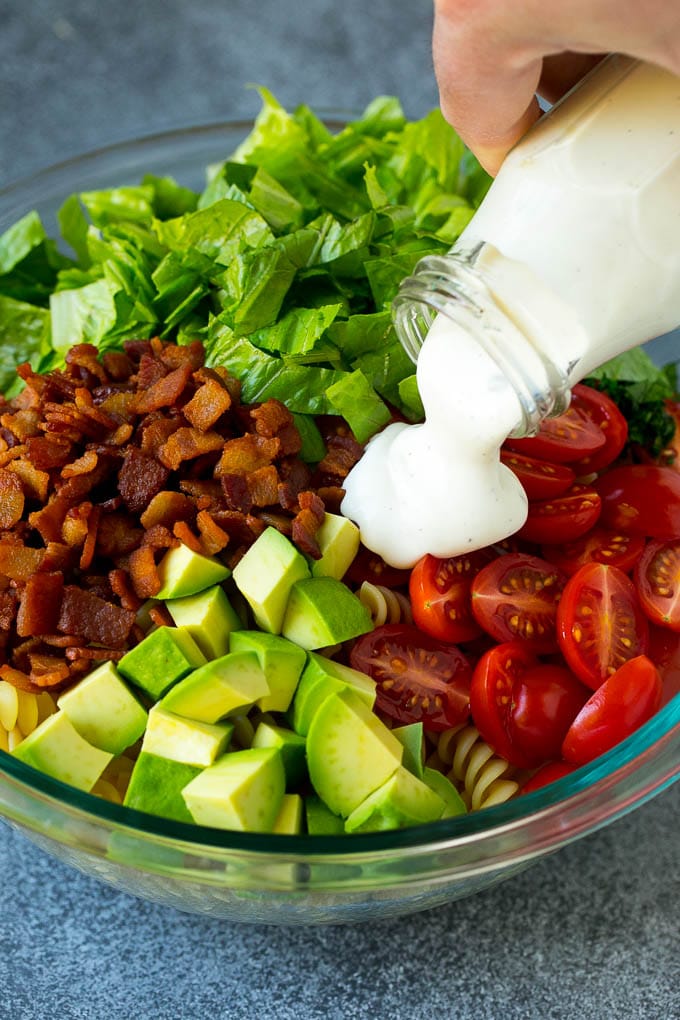 Ranch dressing being poured over tomatoes, lettuce, bacon and avocado.