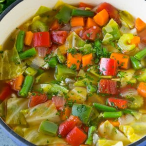 A pot of cabbage soup with carrots, celery, bell peppers and green beans.