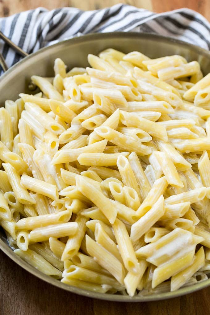 Penne pasta tossed with cream sauce in a skillet.