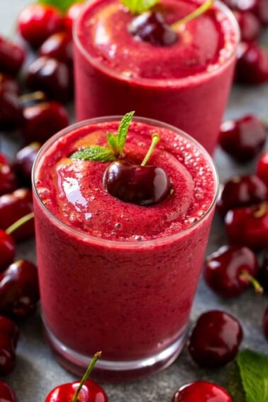 A cherry smoothie garnished with a fresh dark cherry and mint.