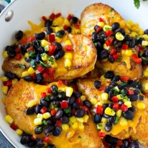 A skillet of chicken Santa Fe which is chicken breasts topped with melted cheddar, black beans, corn and red bell peppers.