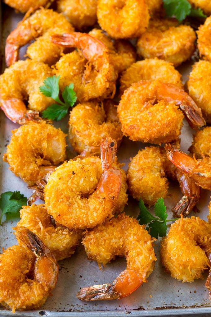 A pile of crispy coconut shrimp on a sheet pan with cilantro leaves for garnish.