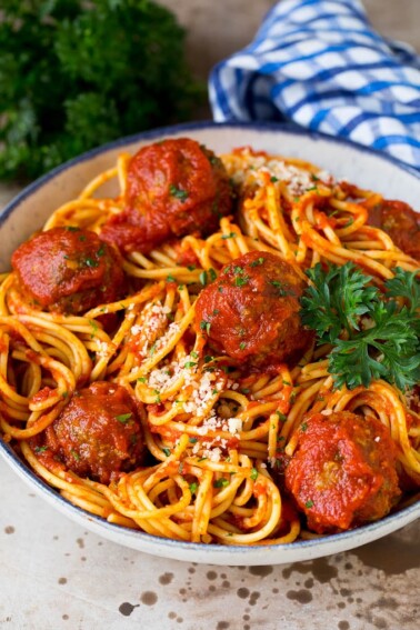 A serving bowl of crock pot spaghetti topped with meatballs and grated cheese.