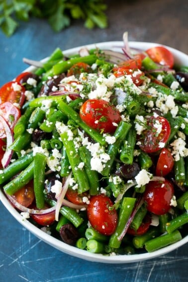 A bowl of green bean salad made with feta cheese, tomatoes, red onion and kalamata olives.