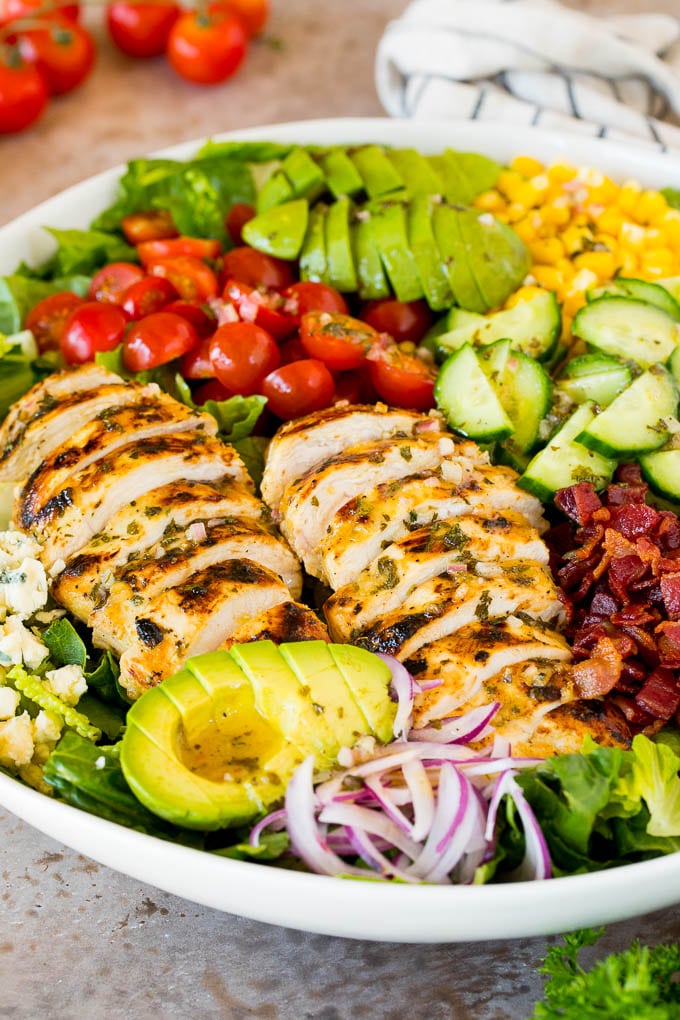 A bowl of grilled chicken salad with tomatoes, avocado and red onion.