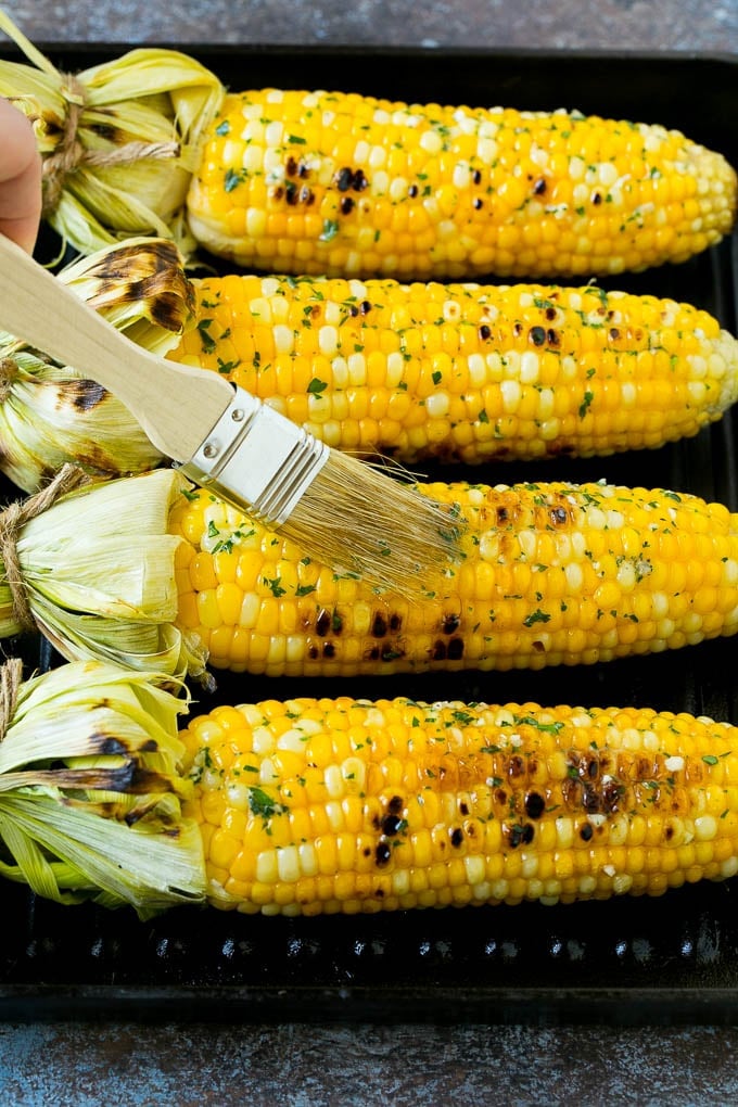 Corn cobs on a grill pan being brushed with herb butter.