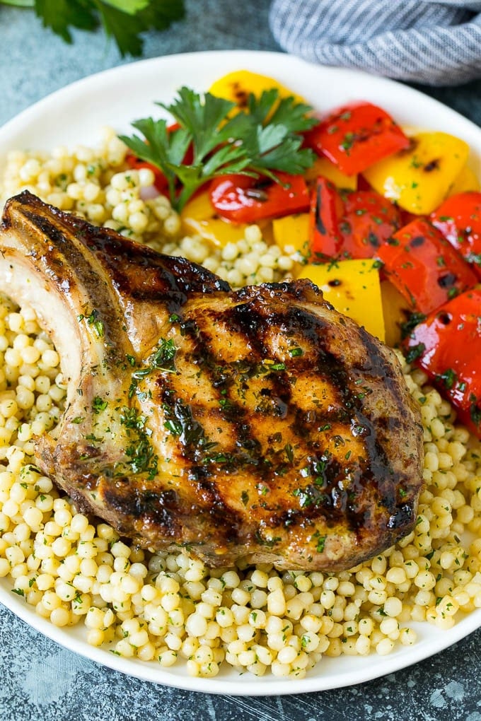 A grilled pork chop served over couscous with bell peppers on the side.