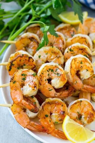 Grilled shrimp skewers with lemon wedges and parsley.