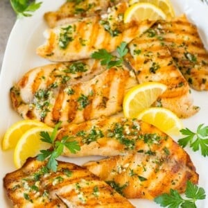 A platter of grilled tilapia fillets garnished with lemon and parsley.