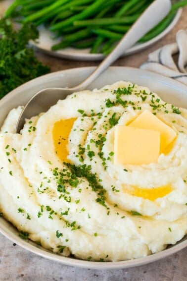 A bowl of make ahead mashed potatoes topped with butter and herbs.