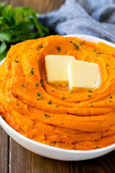 A bowl of mashed sweet potatoes topped with butter and parsley.