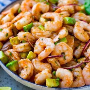 A serving bowl of Mexican shrimp cocktail which contains small shrimp, diced avocado, herbs and jalapeno.