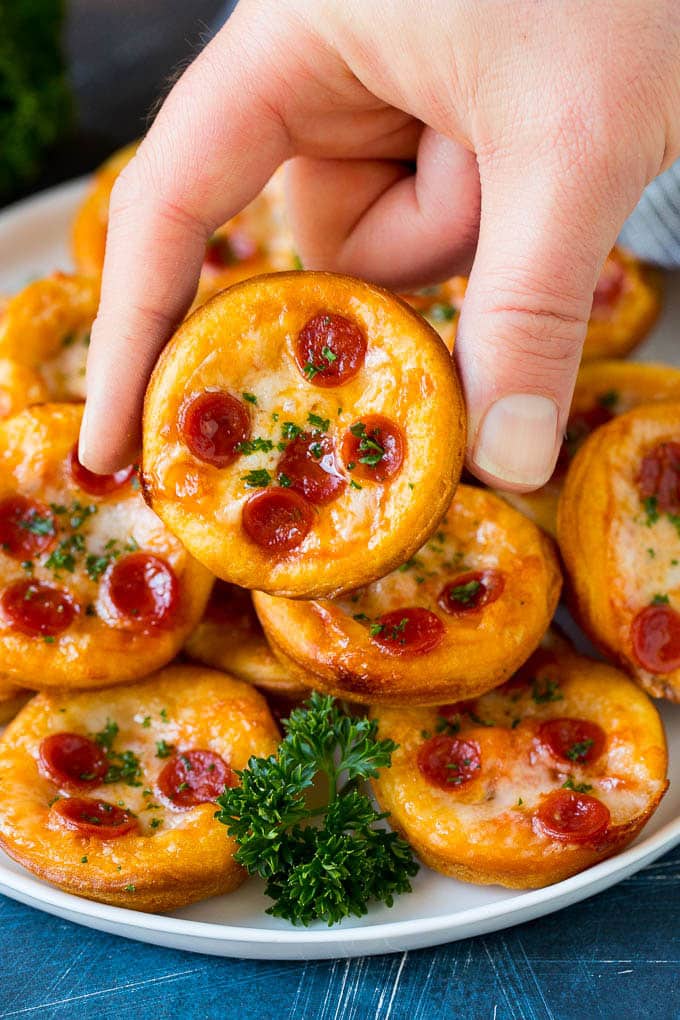 A platter of mini pizzas with a hand reaching for one.