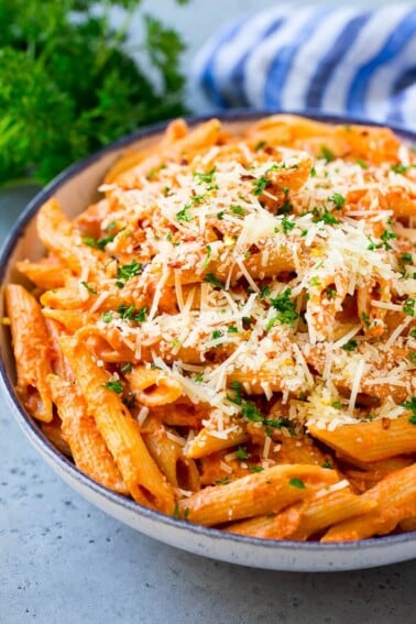 A bowl of penne alla vodka pasta topped with parmesan cheese, parsley and red pepper flakes.