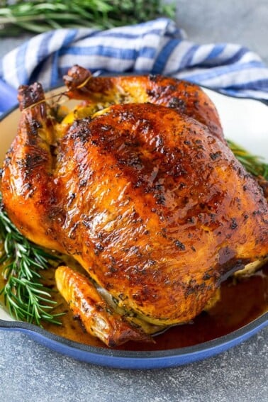 A roasted chicken in a pan garnished with fresh rosemary sprigs.