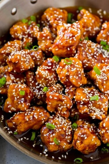 Crispy sesame chicken in a pan, coated in a sweet and savory sauce and sesame seeds.