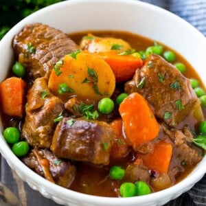 A bowl of slow cooker beef stew with meat, carrots, potatoes and peas.