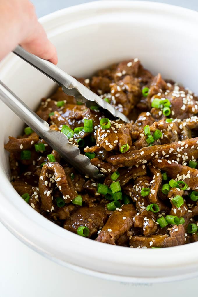 A crock pot of Korean beef with serving tongs in it.