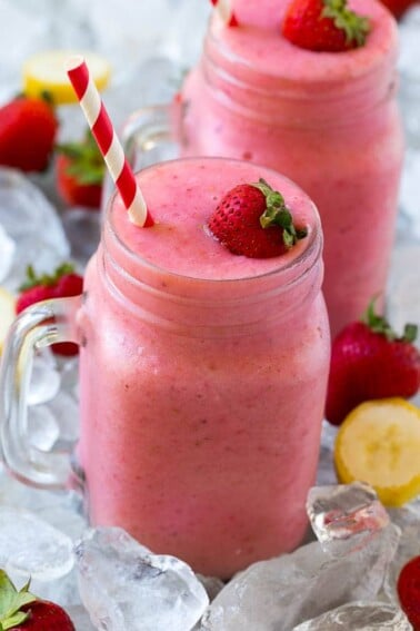 A mason jar mug of strawberry banana smoothie with fresh strawberry on top.