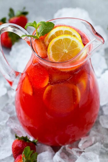 A pitcher of strawberry lemonade garnished with sliced lemons and mint.