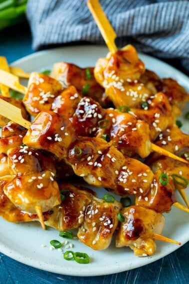 A plate of grilled chicken yakitori topped with sesame seeds and green onions.